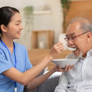 A female caregiver feeding an old man