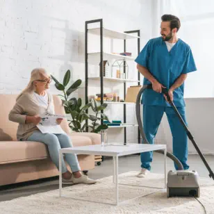A male caregiver cleaning the room of an old woman