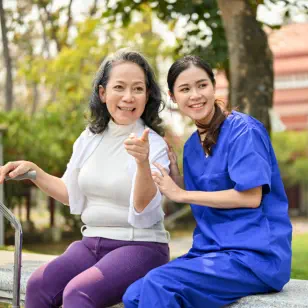 An old woman pointing at something and a female caregiver smiling