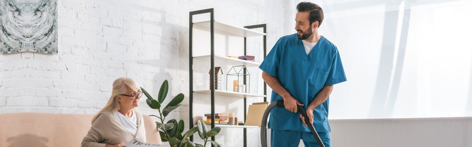 A male caregiver cleaning the room of an old woman