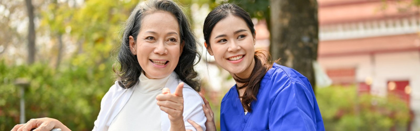 An old woman pointing at something and a female caregiver smiling
